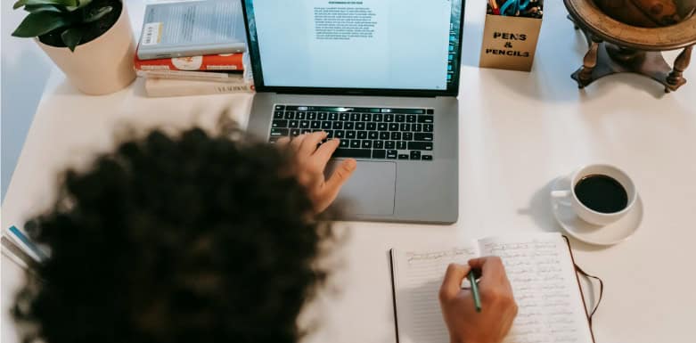 Como produzir conteúdos de qualidade? Conheça o processo de criação da Gear SEO Imagem de pessoa digitando em computador e escrevendo em caderno