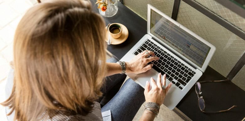 Erros mais comuns em SEO Mulher digitando num notebook, que está ao lado de uma xícara de café.