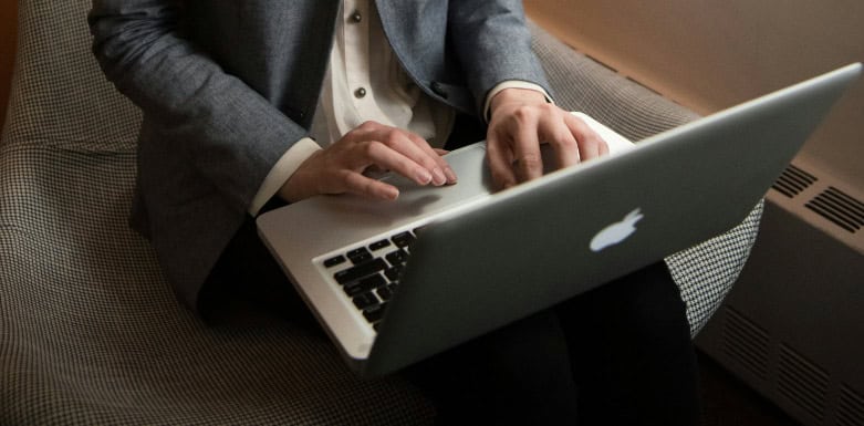 Erros mais comuns em SEO Homem de blazer cinza e camisa branca usando um notebook, que está em seu colo.