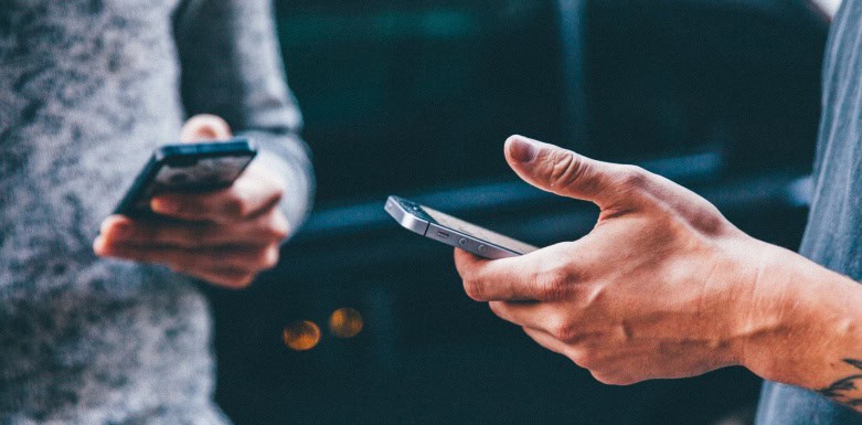 Tempo de permanência: entenda a relevância desse fator para o SEO Duas pessoas segurando celulares em suas mãos.