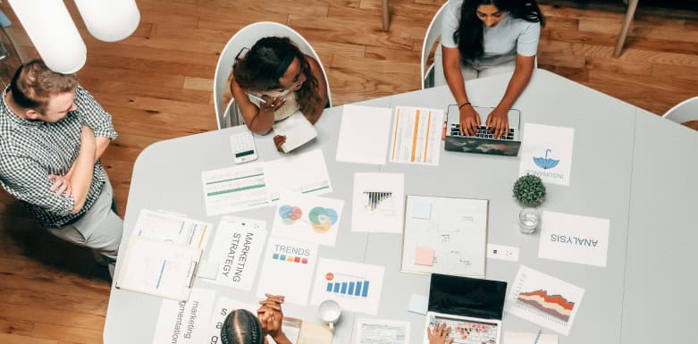 SEO e UX: conheça mais sobre as duas práticas! Equipe avaliando resultados em folhas impressas, espalhadas na mesa.