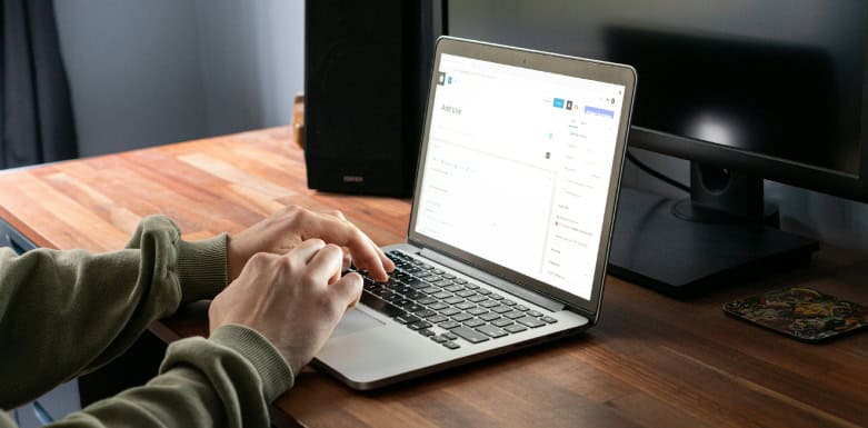 SEO inclusivo: técnicas para criar um conteúdo acessível e relevante Pessoa criando post em blog num computador, que está em cima de uma mesa de madeira.