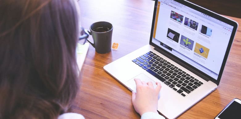 Carregamento assíncrono: conheça mais sobre o assunto! Mulher com a mão no cursor do notebook, ao lado de xícara com chá.